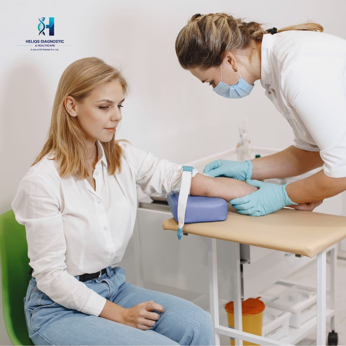 A female healthcare professional in a white coat and mask drawing blood from a patient's arm in a clinical setting.